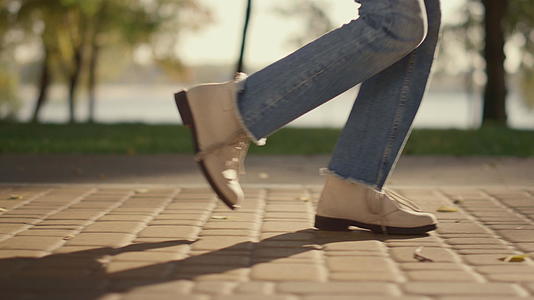 调皮的女孩双腿走在阳光明媚的石板路公园里在特写镜头后留下阴影视频的预览图