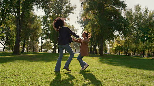 微笑的母亲和女儿一起在绿色的春天公园里跳舞视频的预览图