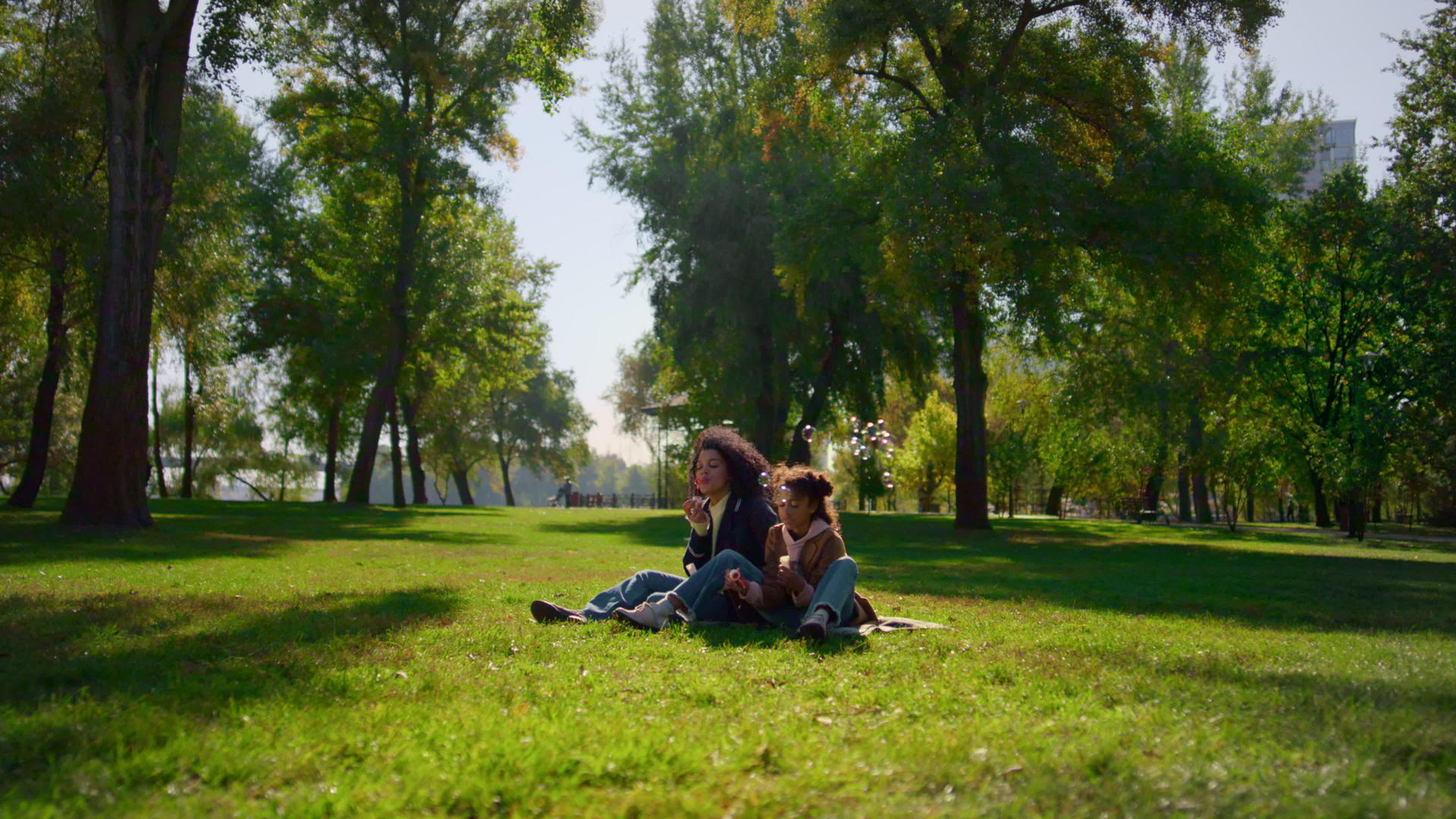 快乐的孩子妈妈在阳光明媚的公园里吹肥皂泡泡视频的预览图