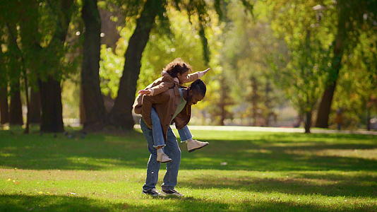 调皮的父亲背着女儿在阳光明媚的公园里享受家庭周末视频的预览图