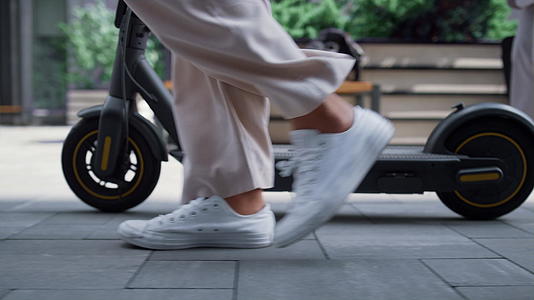 早晨用电动滑板车在市中心街道上行走的特写女性腿部视频的预览图