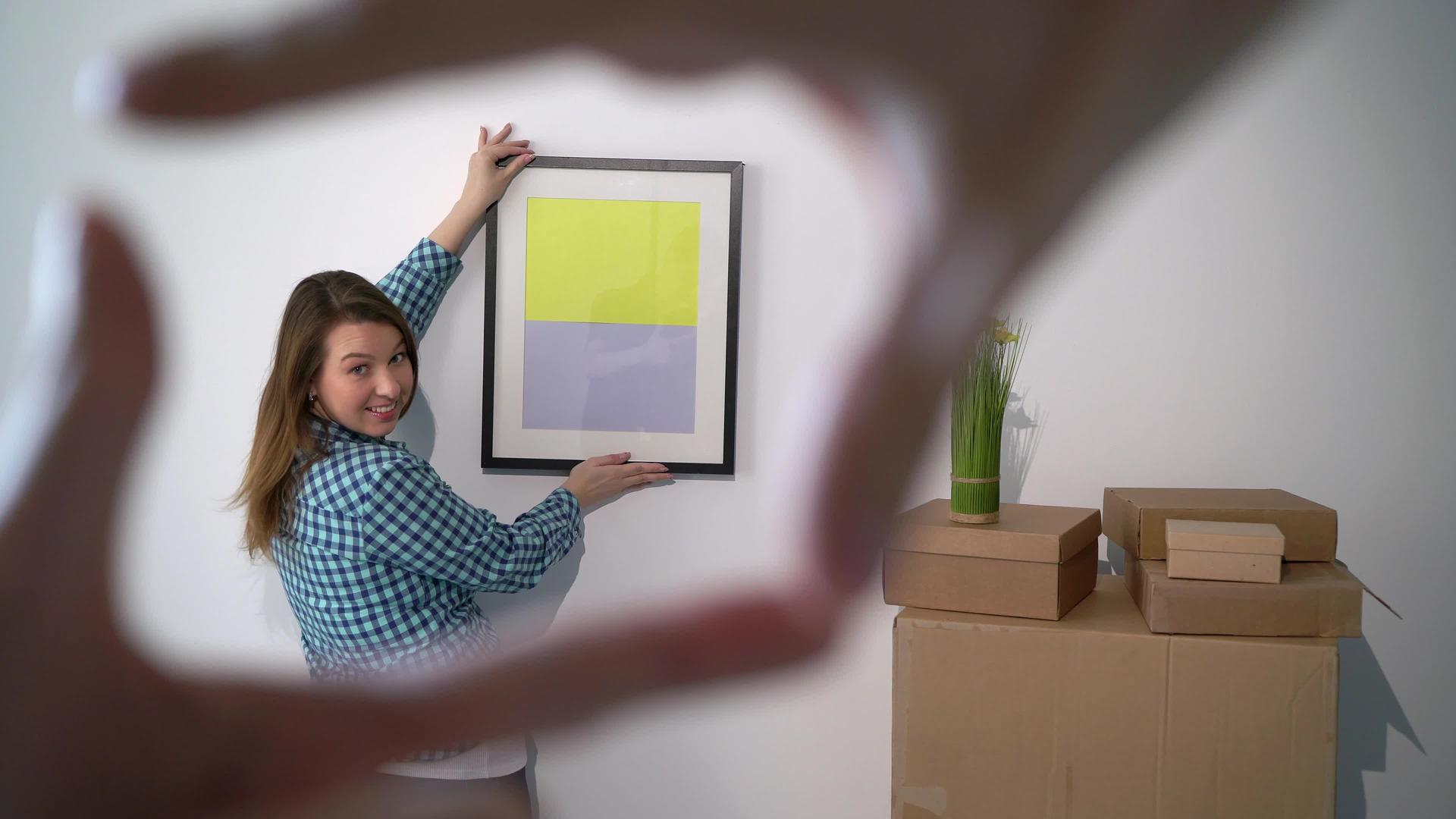 女孩把照片挂在墙上搬进新公寓或新房子视频的预览图