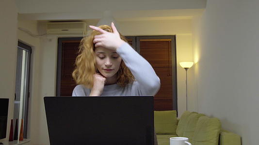 可爱的女孩坐在客厅的桌子上在家里的笔记本电脑前喝咖啡视频的预览图