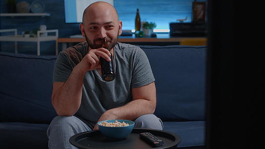 一个人坐在客厅舒适的沙发上吃爆米花喝啤酒视频的预览图