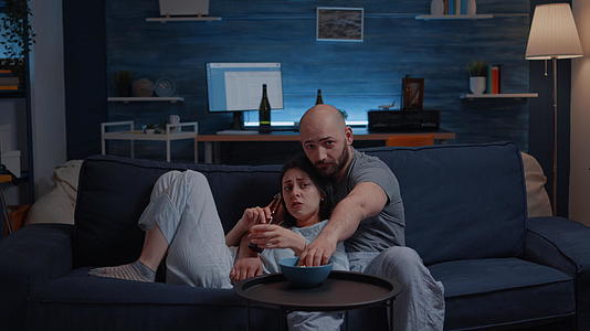 穿着睡衣的情侣坐在沙发上吃爆米花、看电视视频的预览图