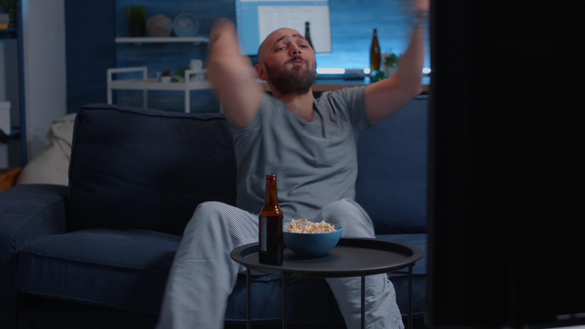 男人用遥控器吃爆米花在电视上看运动视频的预览图