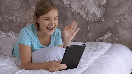 吸引人的金发女孩躺在床上在网上聊天视频的预览图