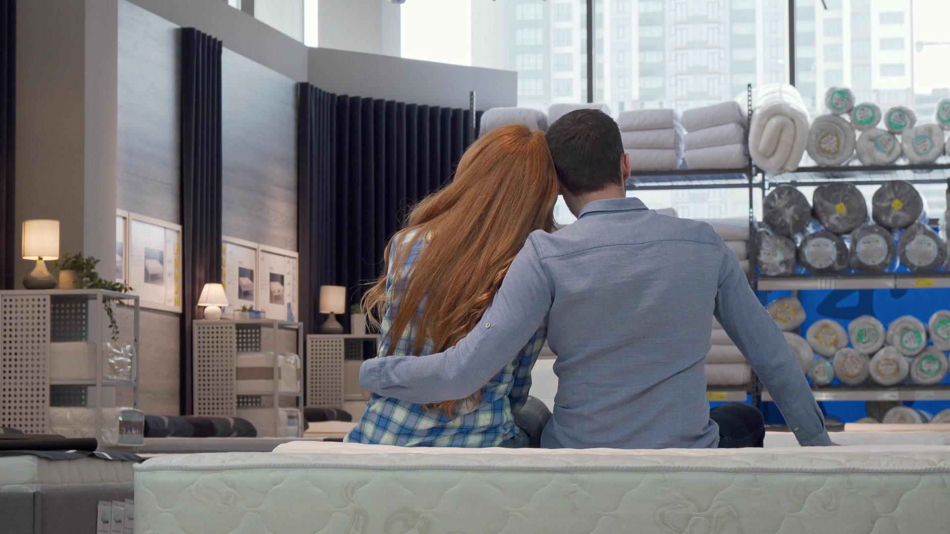 一对夫妇在家具店的新床上拥抱后视镜头视频的预览图