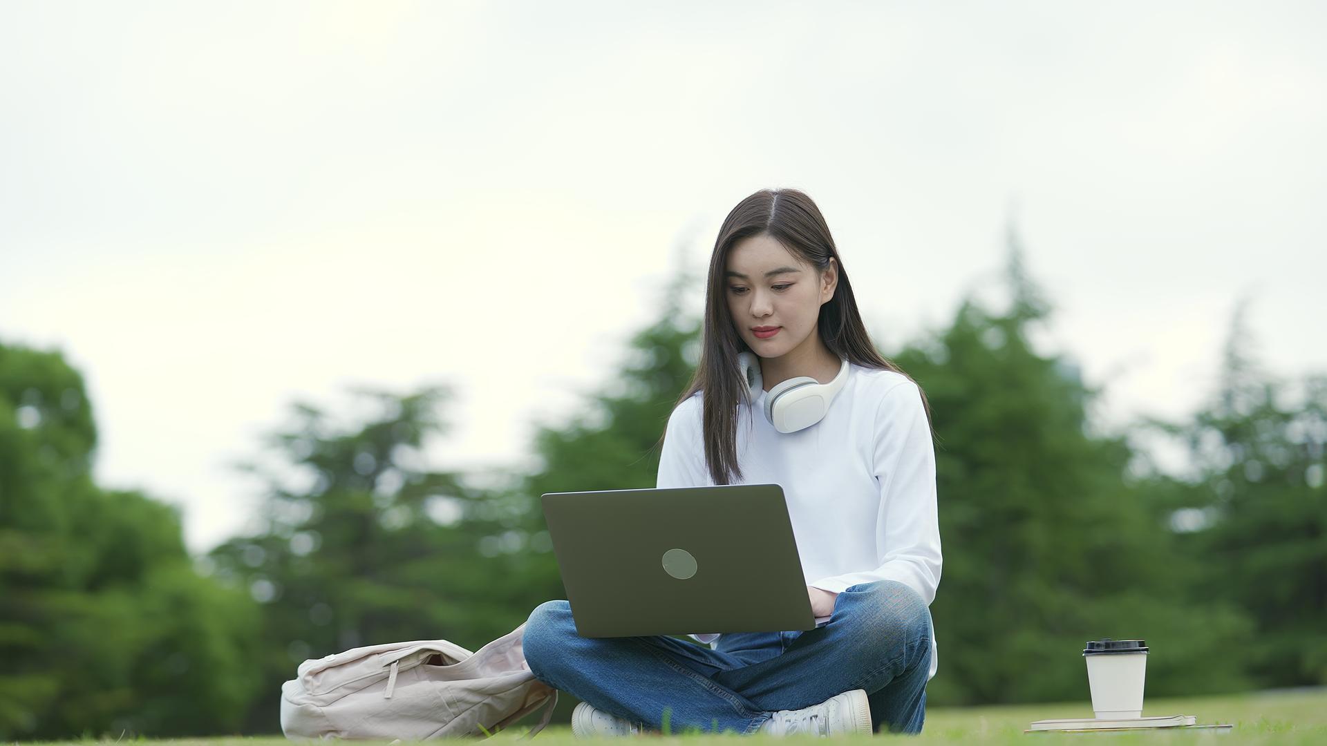 校园女生坐在草地上用电脑视频的预览图