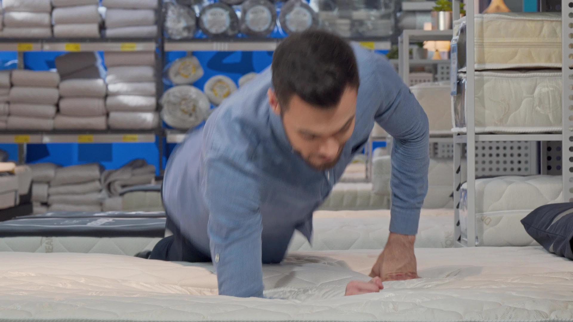 英俊的男人选择塑料床垫躺在商店的新床上视频的预览图