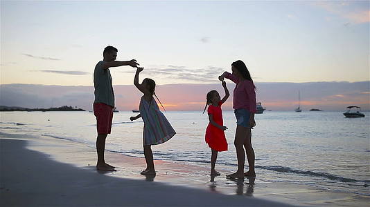 父母和两个孩子在日落的海滩上玩得很开心四个家庭相爱了视频的预览图