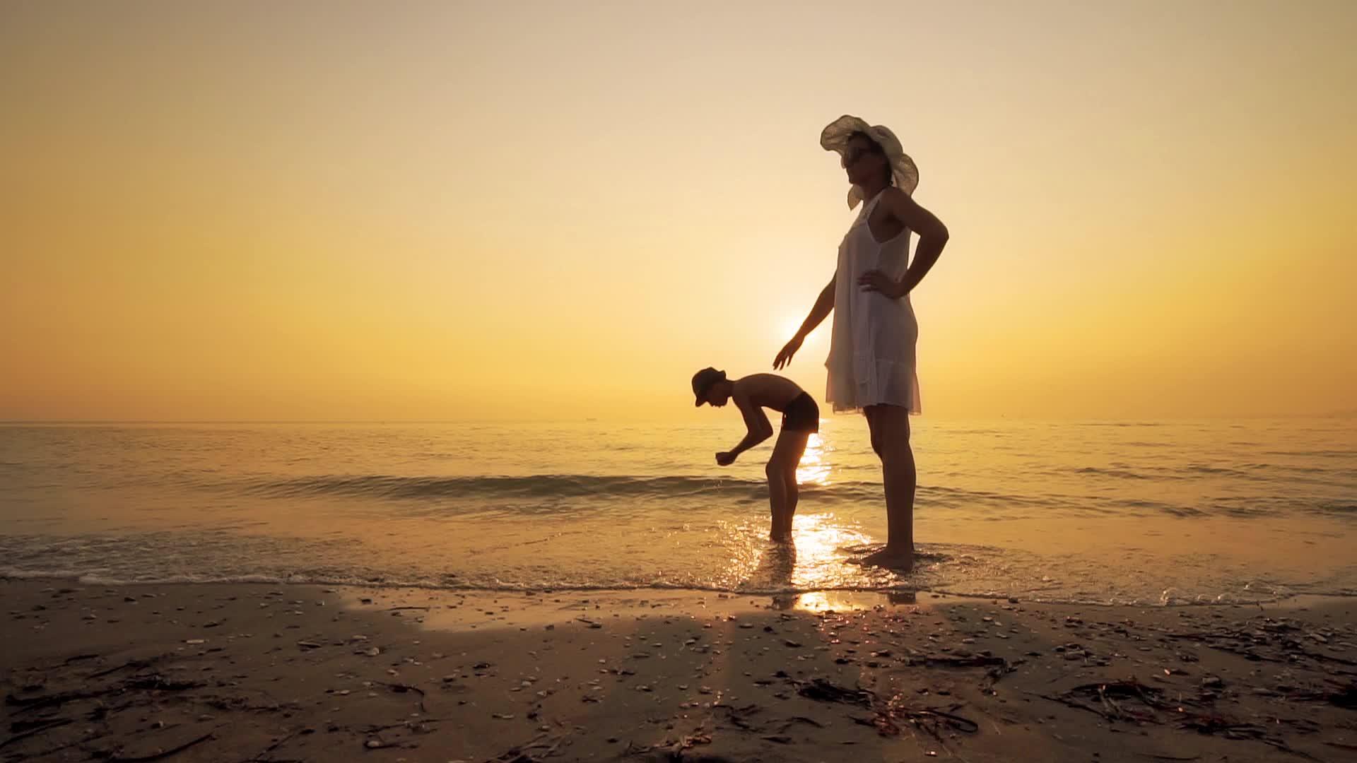 母亲和儿子在日落时在海滩上慢慢移动视频的预览图
