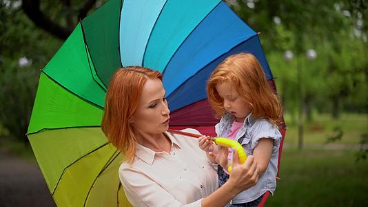 快乐的母亲和女儿在五颜六色的雨伞下视频的预览图