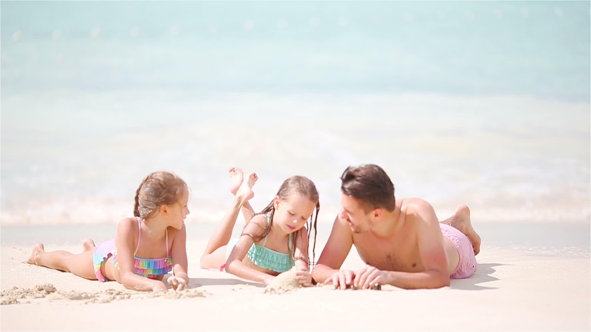 孩子们和他们的父亲躺在浅水里在白色的海滩上玩得很开心视频的预览图
