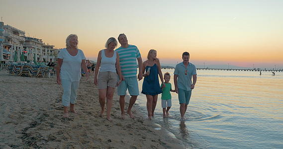 快乐的大家庭在海滩上散步日落背景比雷埃乌斯视频的预览图