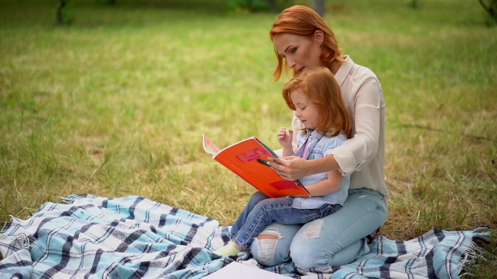 快乐的年轻母亲和女儿在户外阅读视频的预览图
