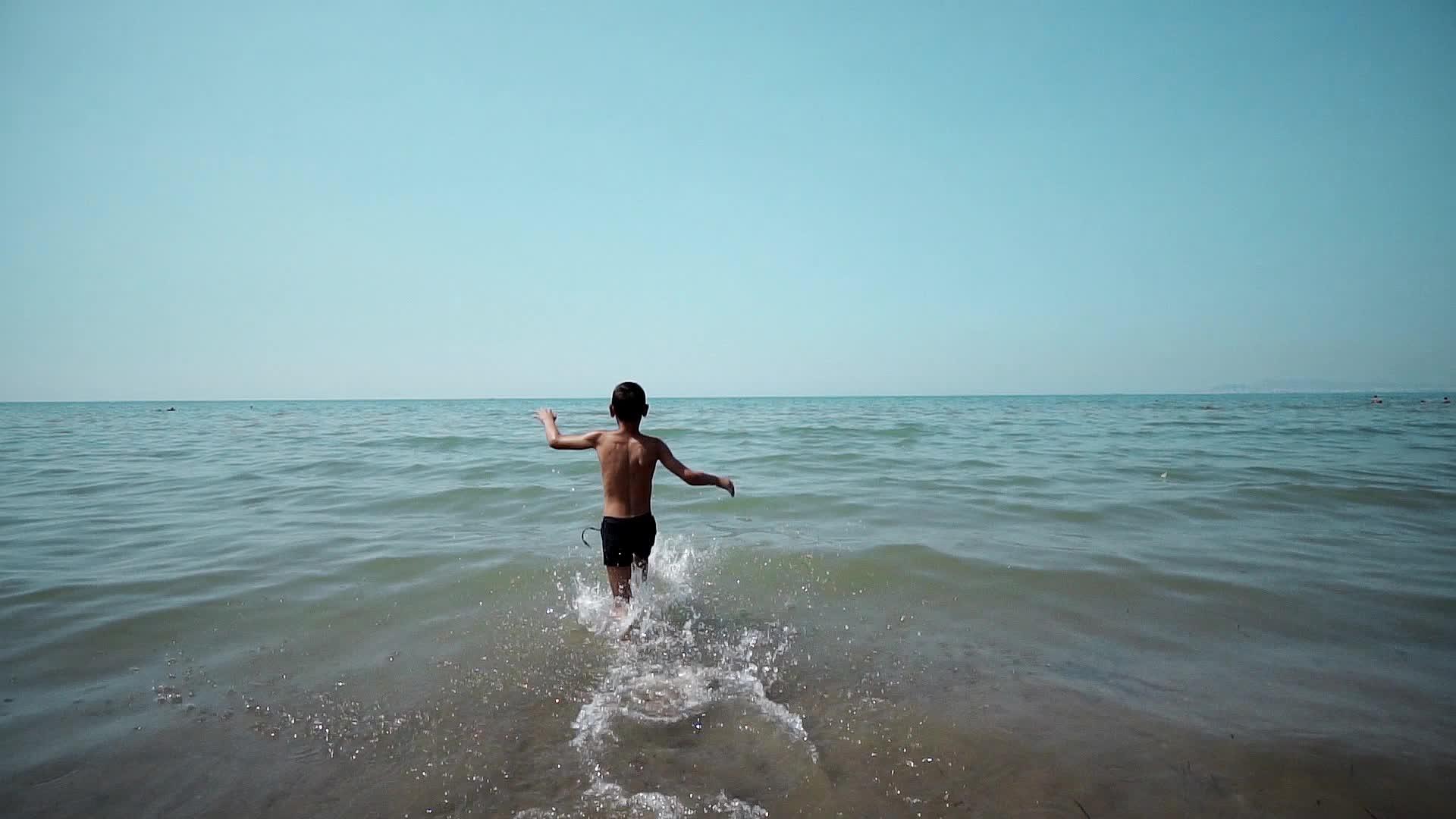 快乐的小男孩在水中奔流在海滩上玩海浪视频的预览图