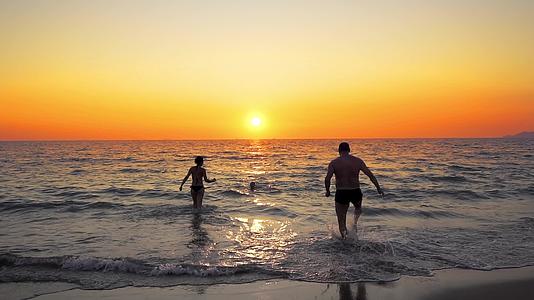 快乐的年轻家庭在日落时在海滩上快乐地奔跑视频的预览图