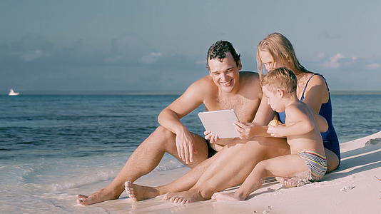 三个幸福的家庭坐在海边用垫子坐着视频的预览图