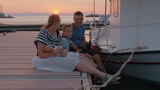 父母、长子和婴儿在日落时坐在码头上视频的预览图