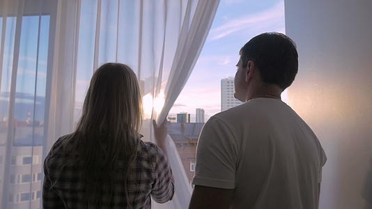 一对年轻夫妇透过窗户看着大城市的窗户视频的预览图