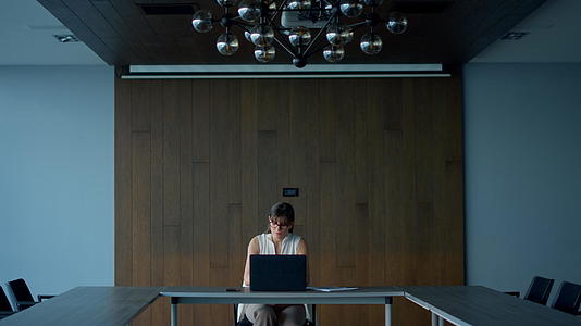 黑发女商务人士独自在空荡荡的会议室里工作笔记本电脑视频的预览图