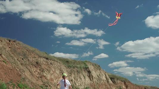 女孩在阳光明媚的夏天在岩石沙滩上玩风筝她控制着蓝天视频的预览图