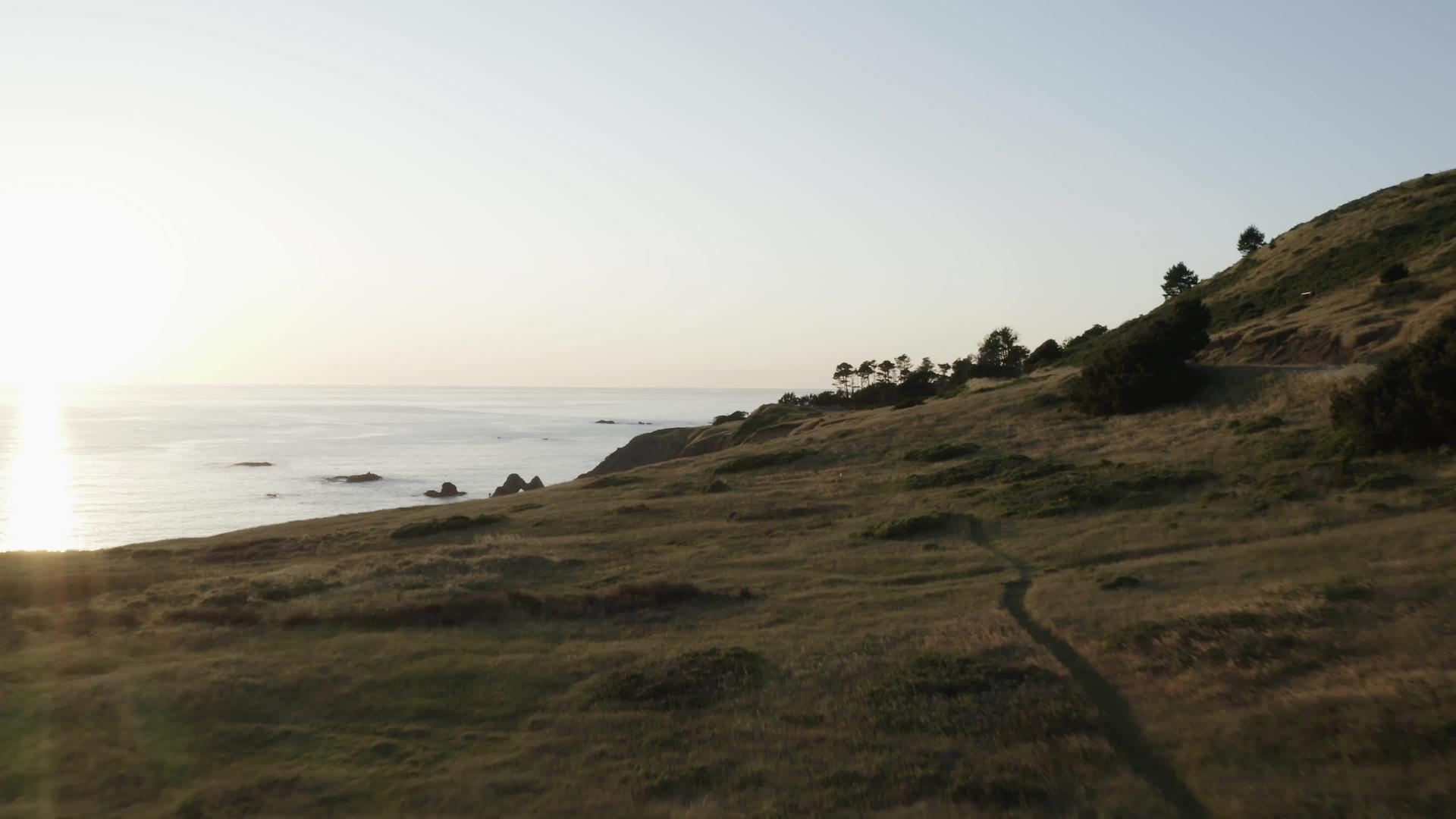 日落时沿着海岸的悬崖和草山坡的足迹被磨损视频的预览图