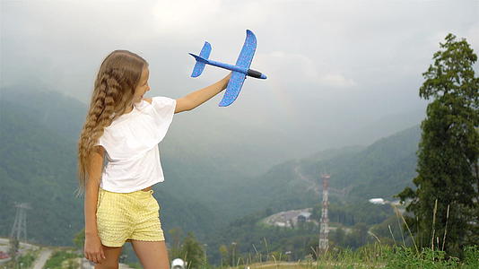 可爱快乐的小女孩在山上美丽的风景背景下玩玩具飞机的快乐视频的预览图