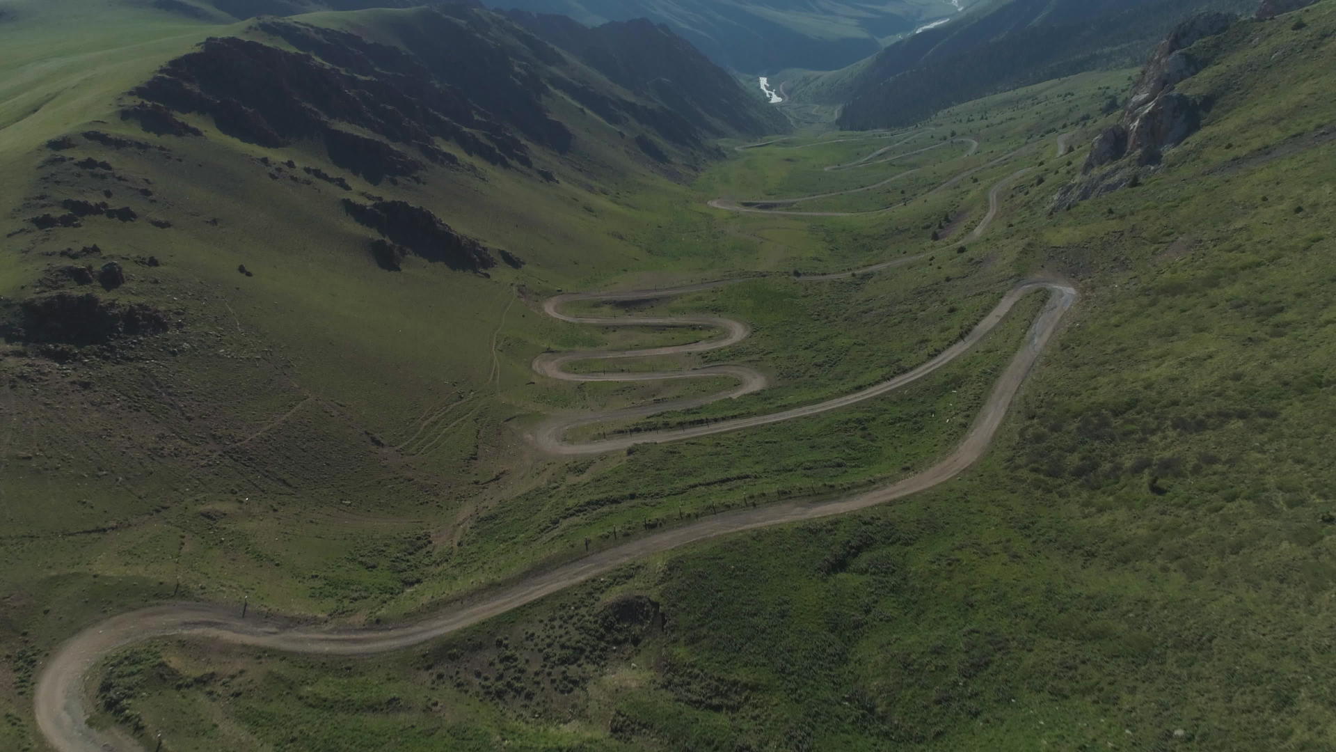 无人机在夏天的山区飞越弯曲的蛇形道路视频的预览图
