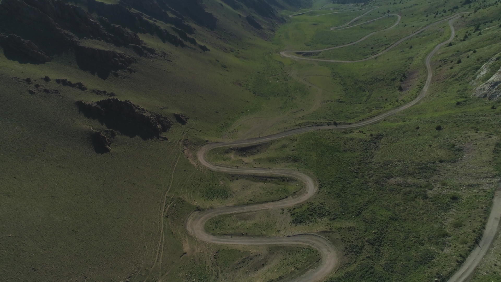 无人机在夏天的山区飞越弯曲的蛇形道路向后飞行视频的预览图