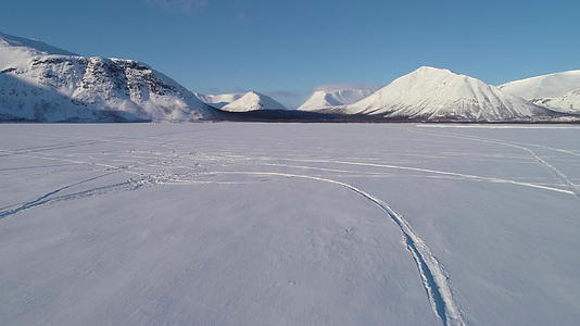 在冬天阳光明媚的日子里无人机低角向前飞越雪湖到山脉视频的预览图