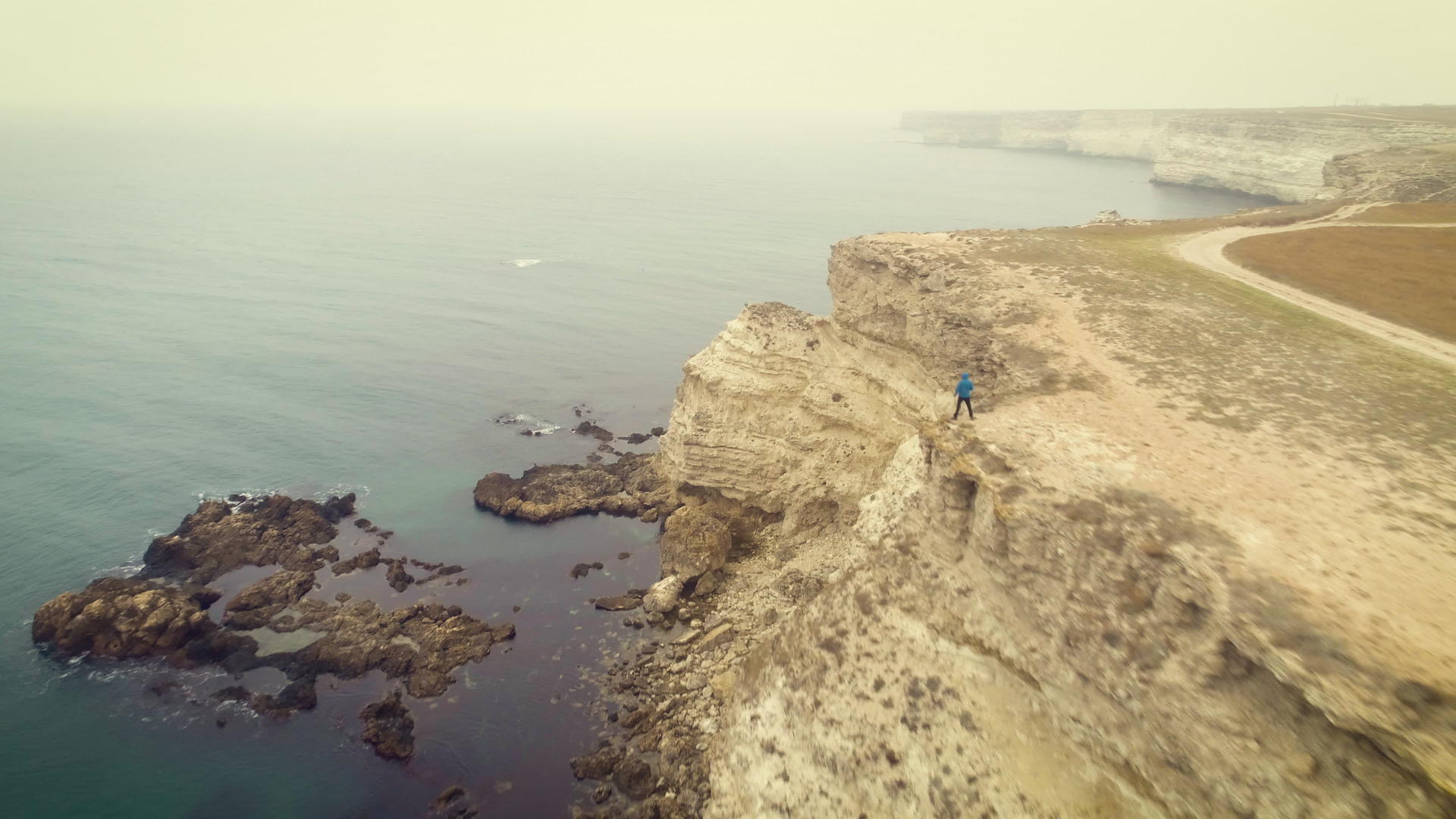 旅行者站在海岸线岩石悬崖边缘的空中观察无人驾驶飞机视频的预览图