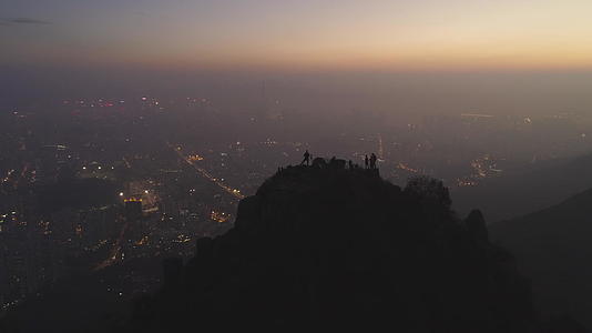 黄昏时分人们在岩石顶部的剪影照亮了城市的天际线视频的预览图