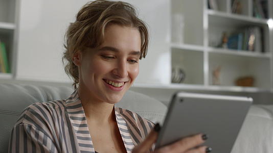 肖像微笑的女人在家里拿着平板电脑看好消息视频的预览图
