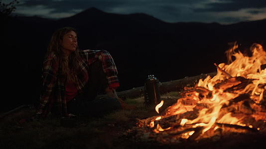 孤单的女人看着篝火在漆黑的夜晚燃烧视频的预览图