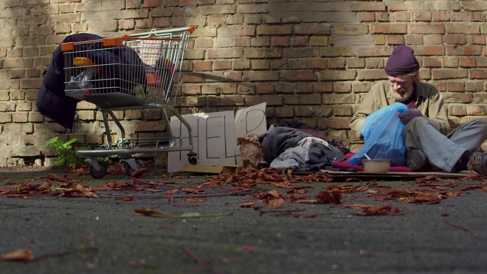 无家可归的人坐在砖墙旁边的纸板上视频的预览图