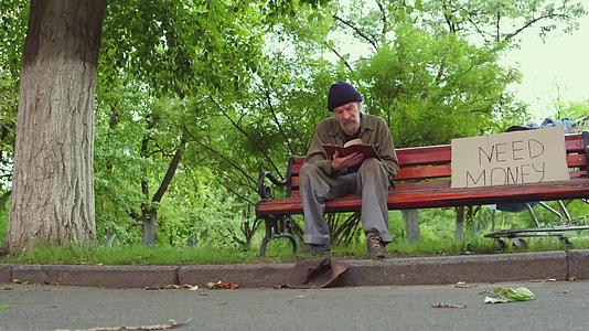 无家可归的老人坐在长凳上手里拿着一本书视频的预览图
