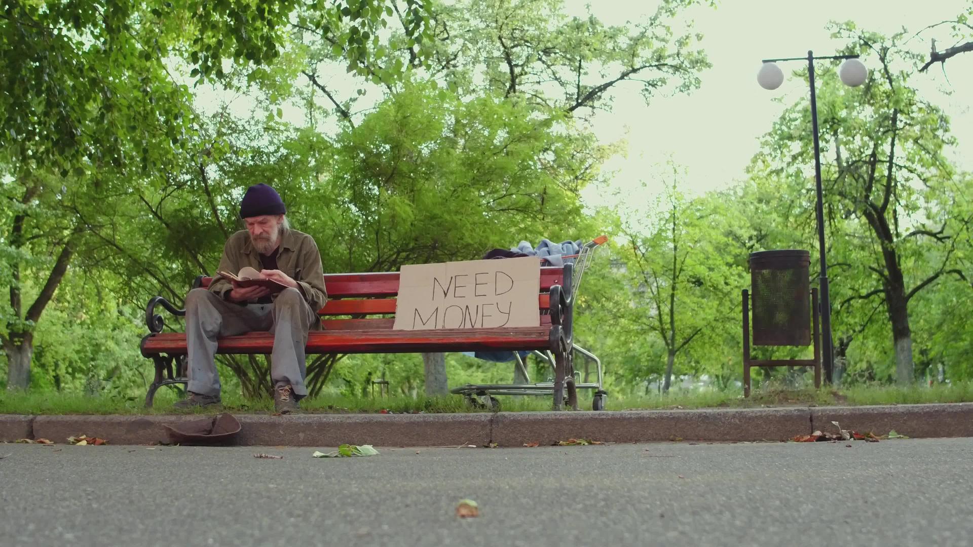 无家可归的人坐在长凳上手里拿着一本书视频的预览图