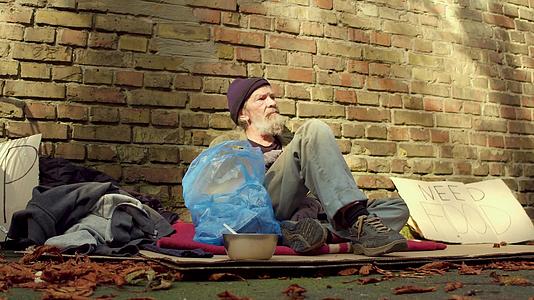 无家可归的人坐在墙砖旁边的纸板上视频的预览图