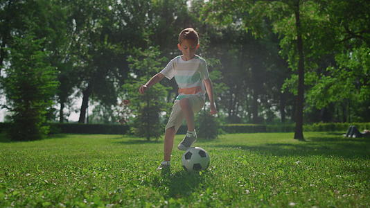 小男孩在公园的草地上做足球运动视频的预览图
