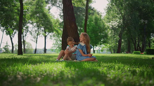 快乐的孩子坐在绿草地上的树附近视频的预览图