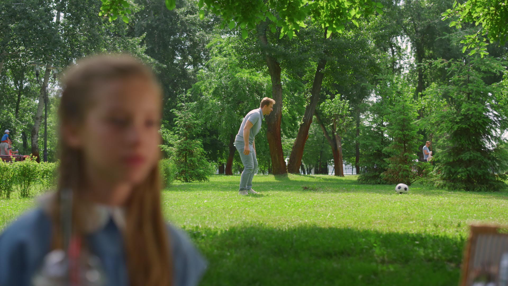 年幼的父亲在公园休息的女儿身后传球给活跃的儿子视频的预览图