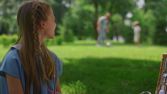 冷静的女孩在绿色草坪特写镜头上观看足球训练父亲和儿子视频的预览图