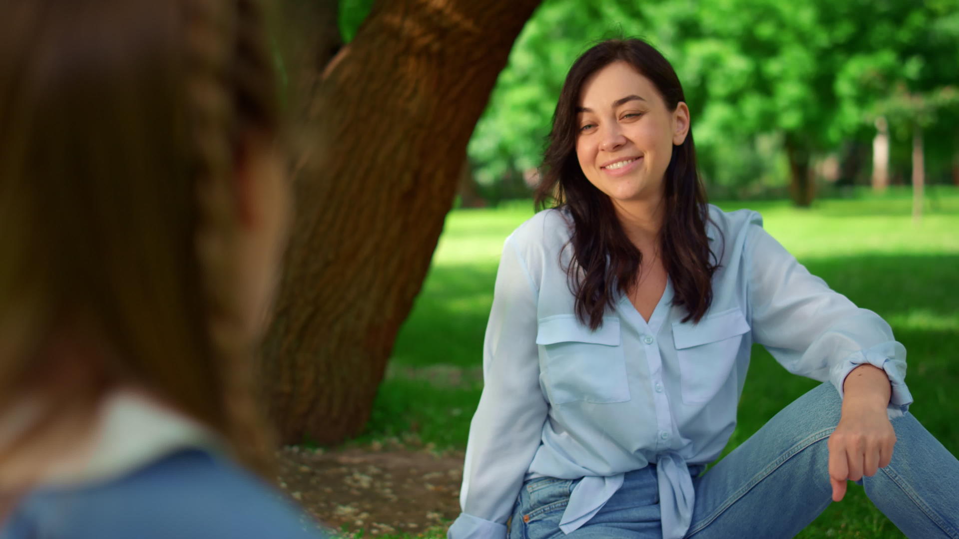 微笑的妇女坐在公园特写镜头的草地上视频的预览图
