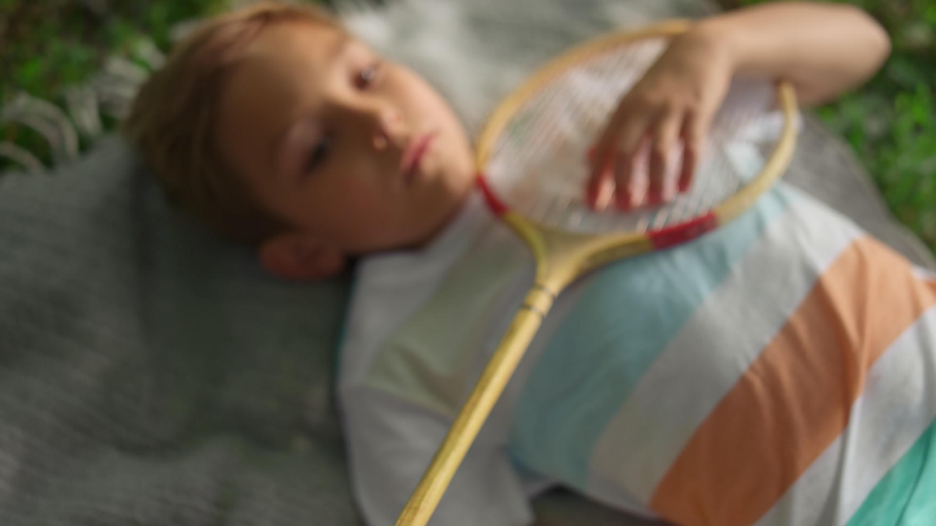 疲倦的男孩躺在毯子上在夏季公园检查羽毛球球拍网视频的预览图