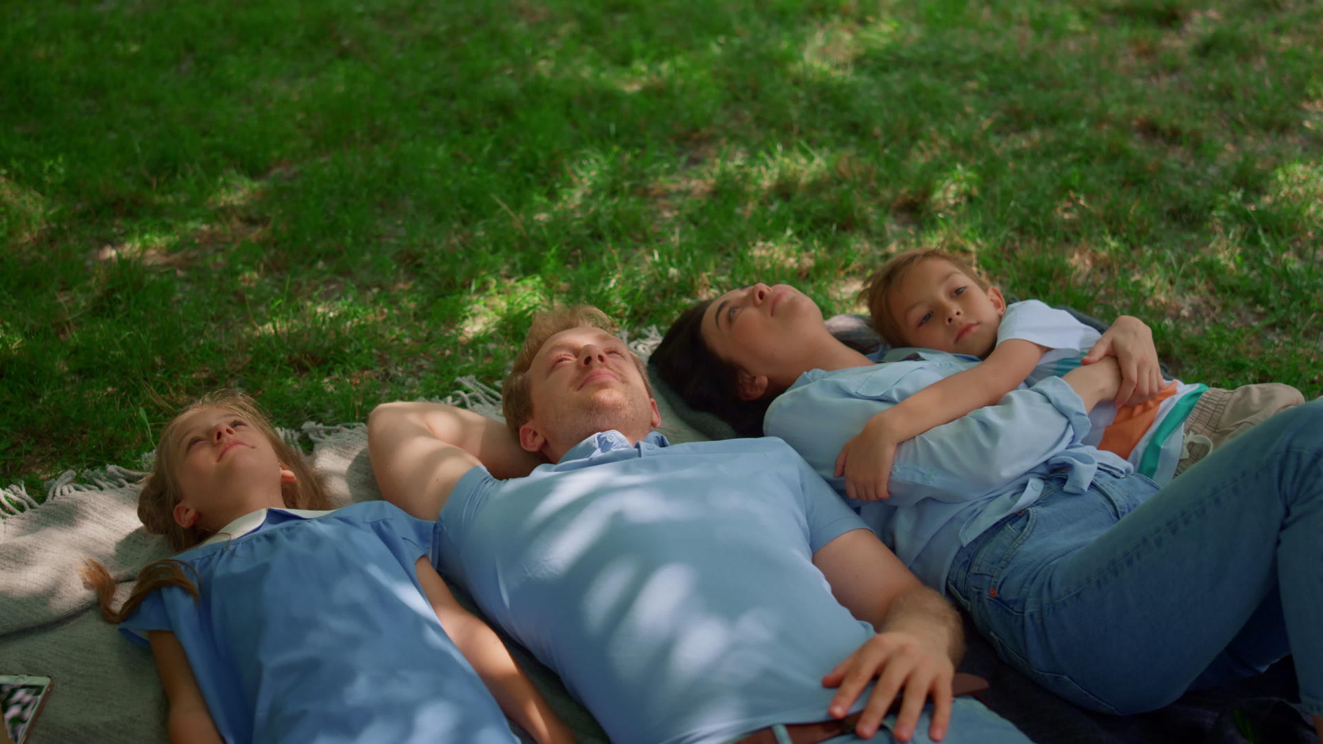 快乐的父母和孩子躺在草地上看着视频的预览图