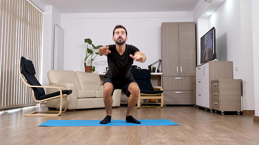 年轻的运动男子蹲在客厅里视频的预览图