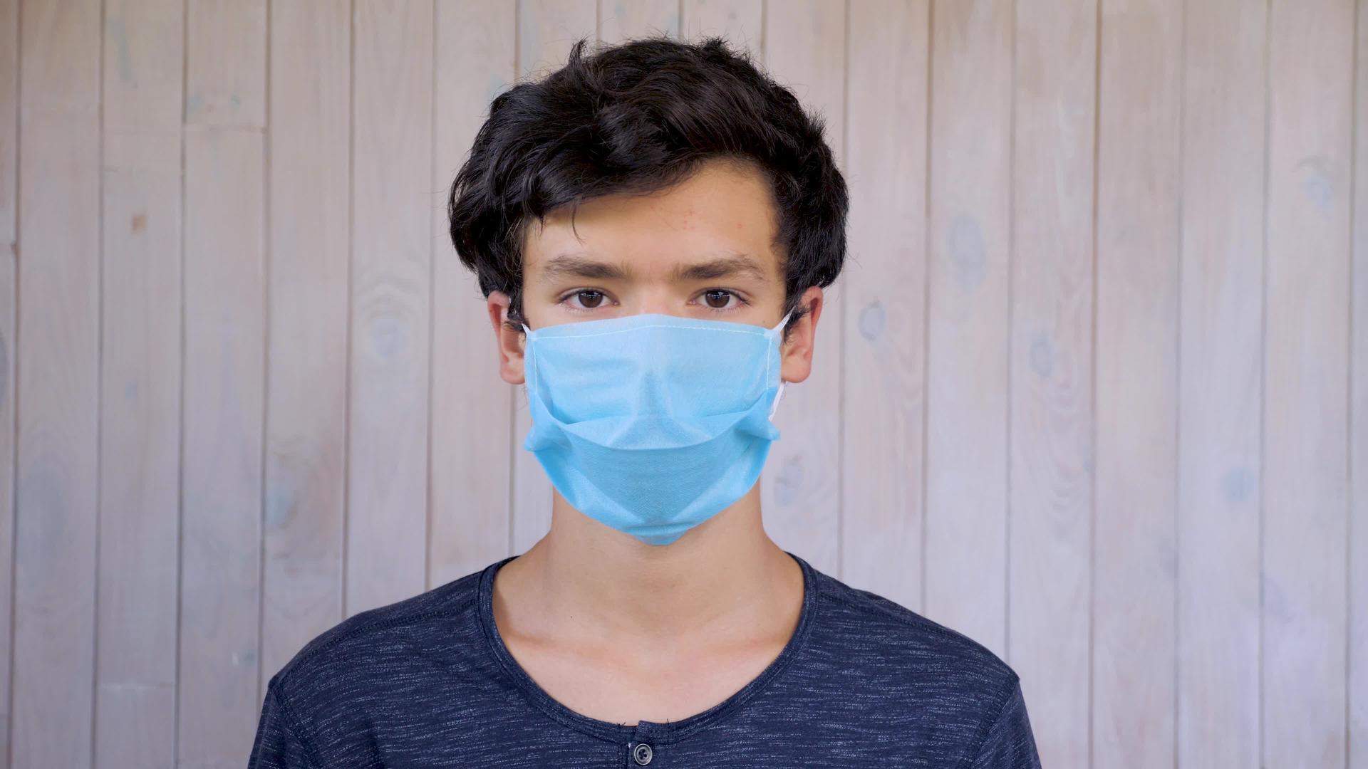 戴着医用口罩的年轻人看着戴着口罩的15岁男孩的相机视频的预览图