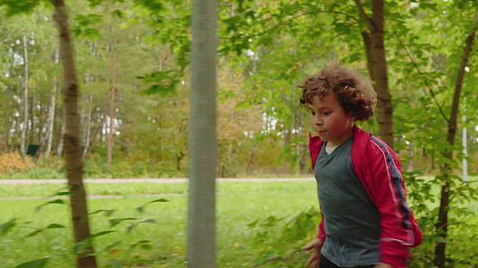 年轻的卷发男孩在夏天公园的小路上快乐地奔跑视频的预览图